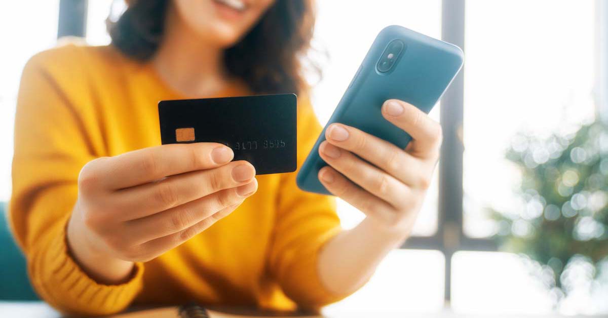 Woman smiling using her phone and holding a credit card