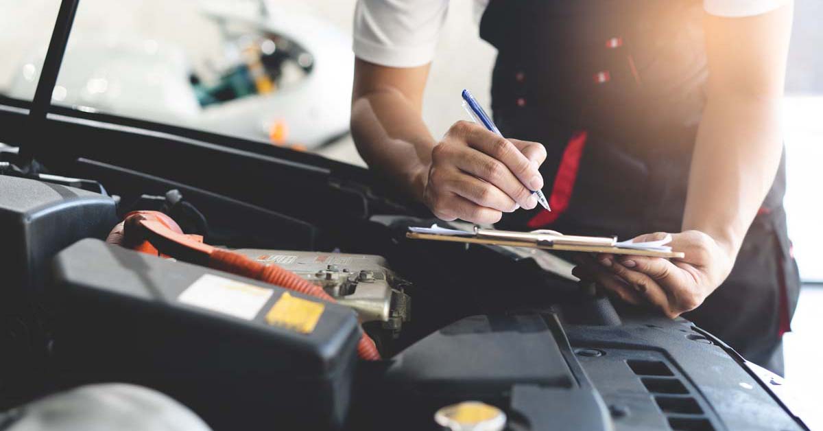 Car mechanic with a clipboard checking the engine of a car