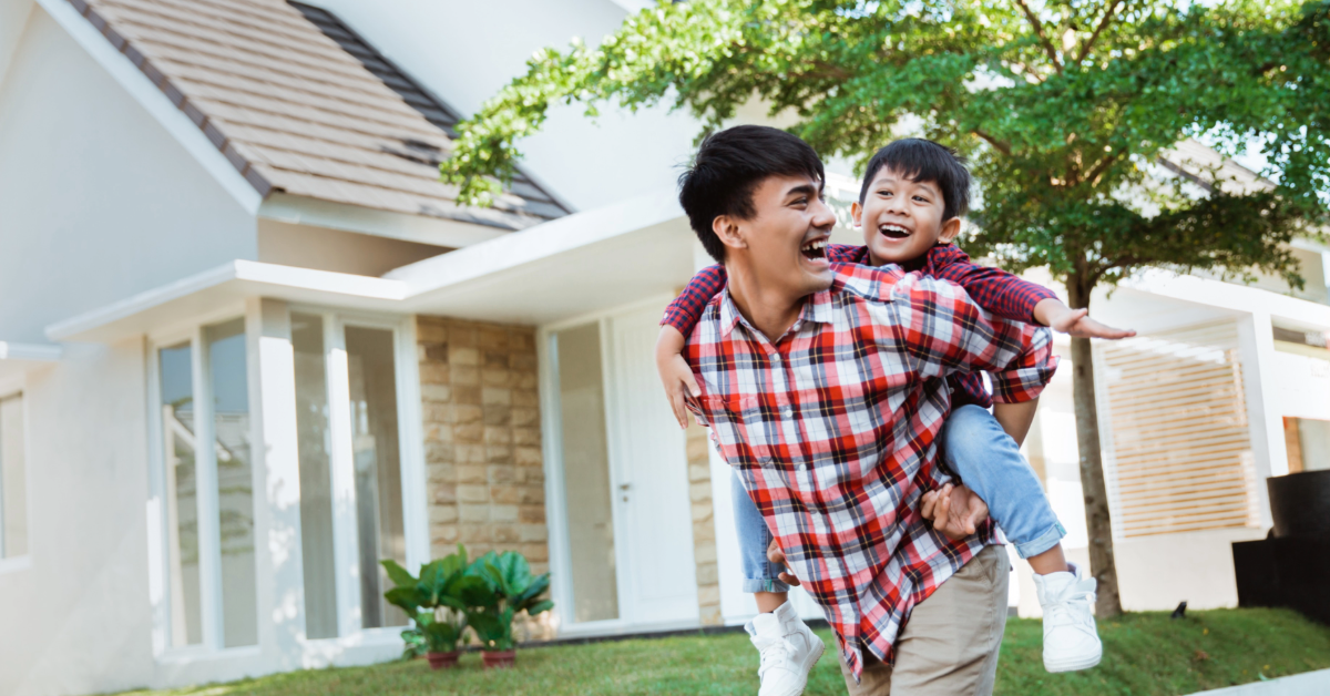 Person giving house keys to another person in front of a green house