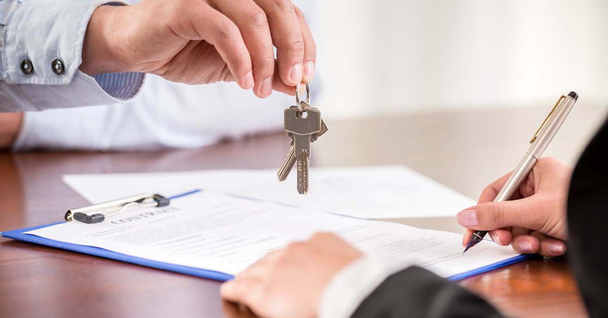 Person giving house keys to another person signing paperwork 