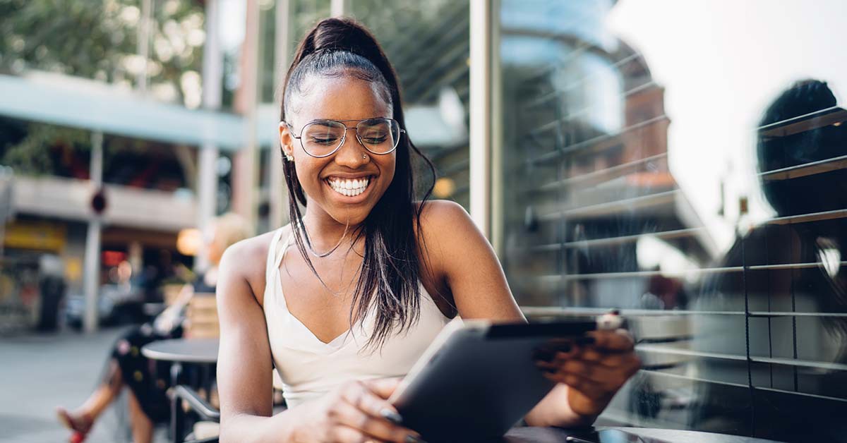 Woman sitting outside of a cafe smiling with a tablet in hand 