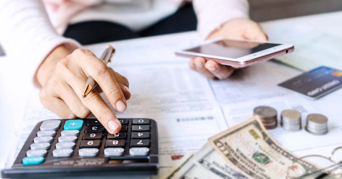 Person making calculations on a calculator while looking at phone with a table of money