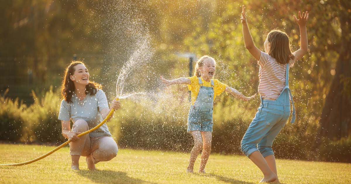 Woman and children outside enjoying summer with a hose