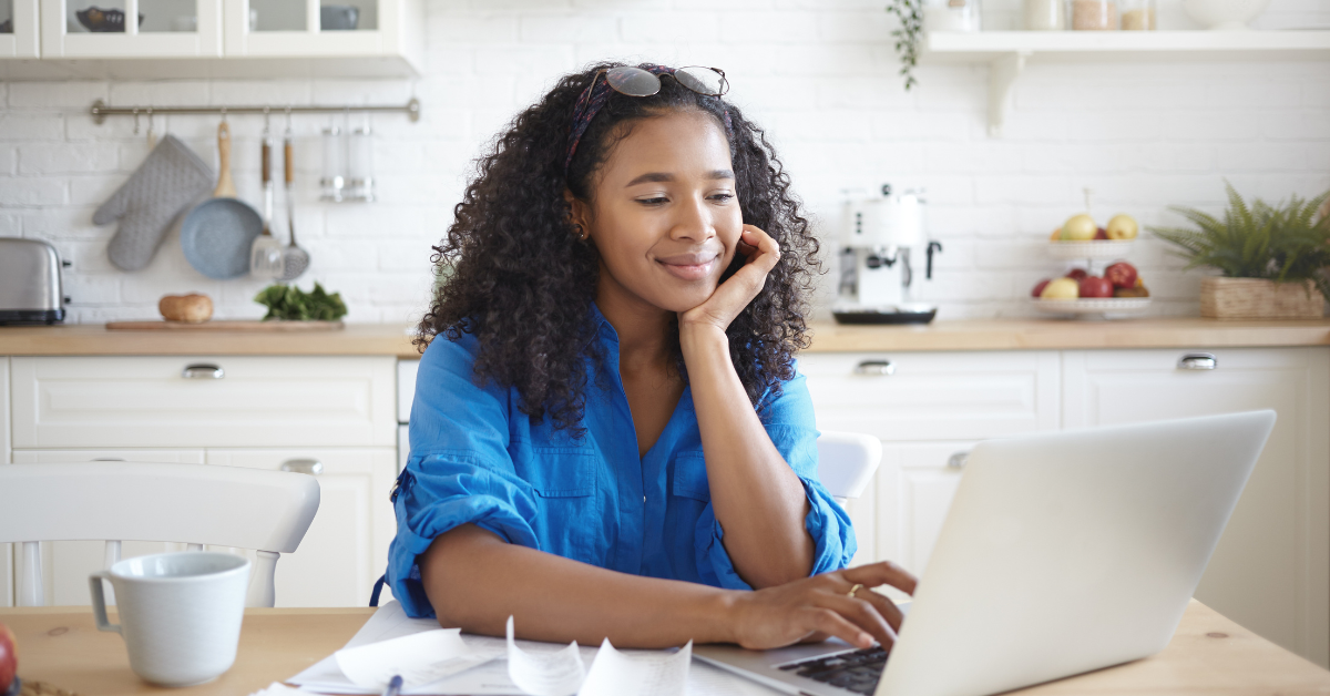 Woman smiling and sitting in kitchen using laptop 