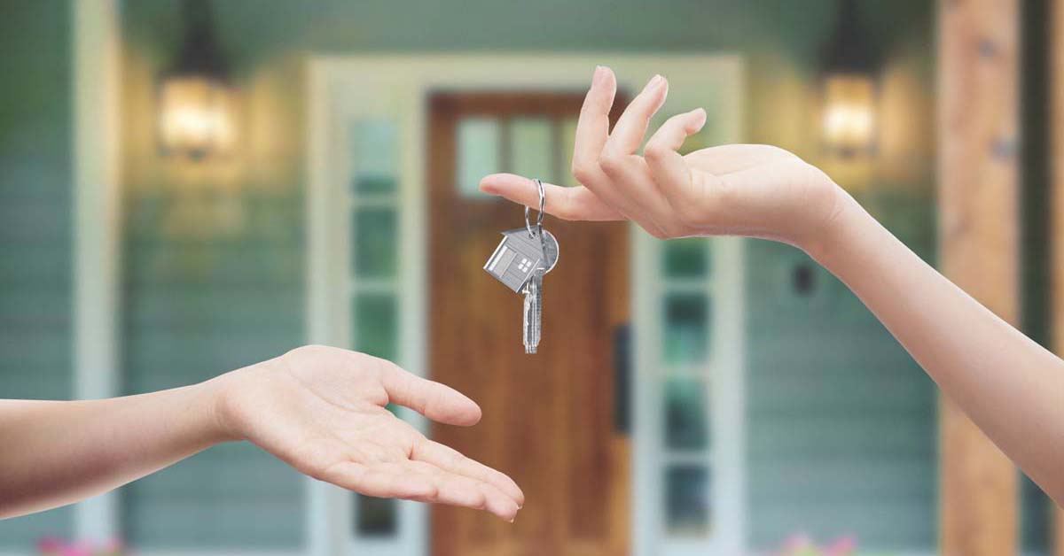 Person giving house keys to another person in front of a green house