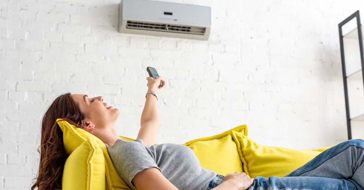 Woman sitting on yellow couch enjoying the air conditioner 